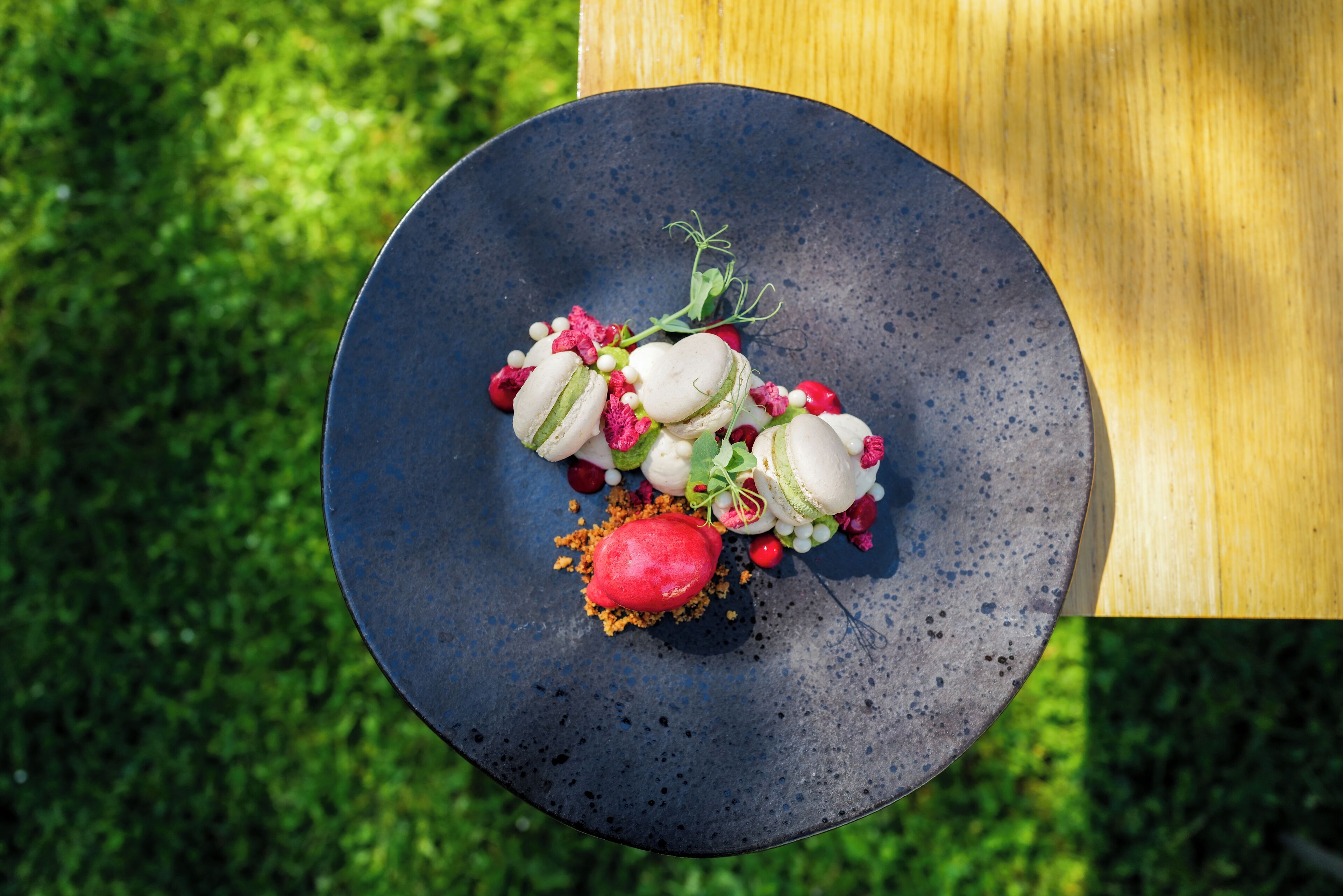 Une assiette noire ronde, sur laquelle se trouve un dessert, est posée sur une table en bois, le tout sur un fond vert.
