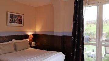 Habitación de hotel con una cama grande, una mesita de noche con lámpara, un cuadro en la pared y vistas al exterior a través de una puerta corredera.