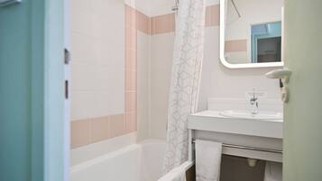 A bathroom with a bathtub, a shower curtain, a sink, and a mirror.