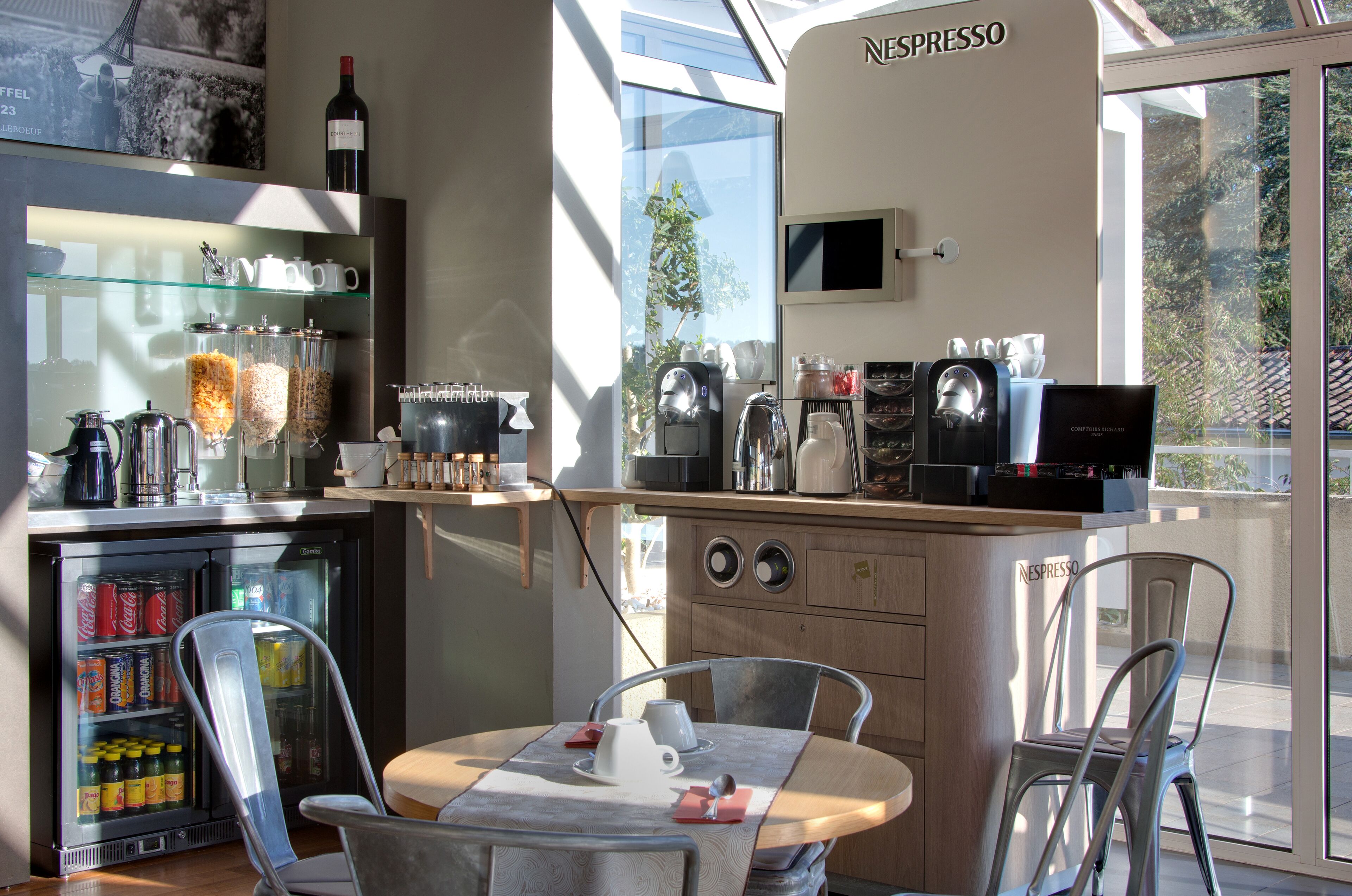 A modern coffee shop with a glass refrigerator, espresso machines, and seating area.
