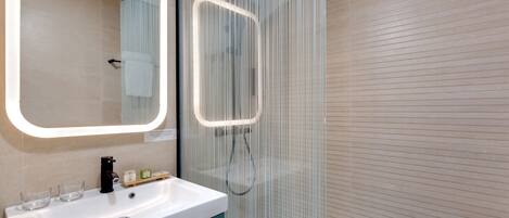 Un baño moderno con lavamanos blanco, un espejo con luz y mampara de ducha de vidrio.