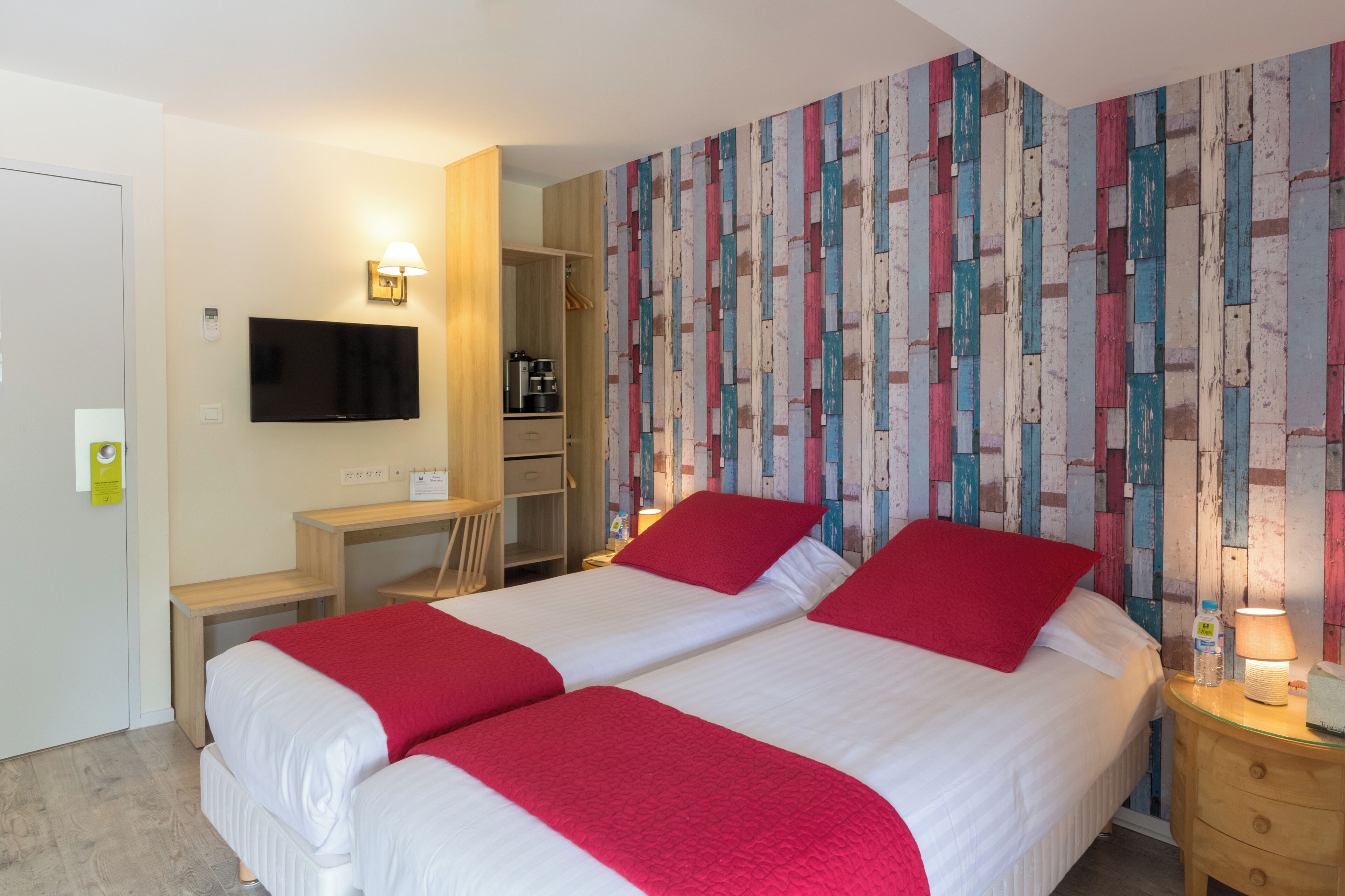 A hotel room with two beds, a desk, a TV, and a wardrobe.