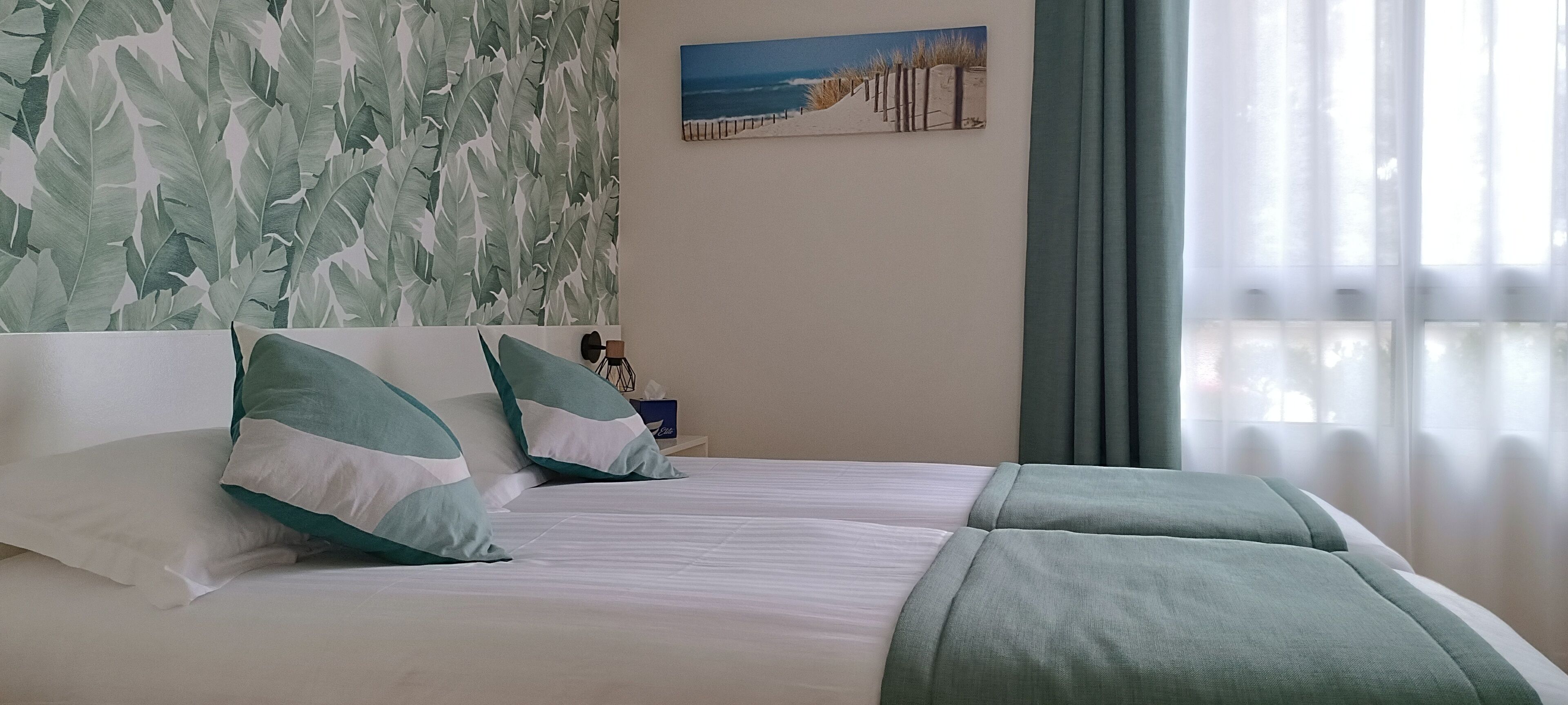 A hotel room with a bed, pillows, a painting, and a window with curtains.
