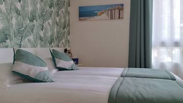 A hotel room with a bed, pillows, a painting, and a window with curtains.