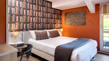 A bedroom with a large bookshelf, a bed with pillows, a desk, and a chair.