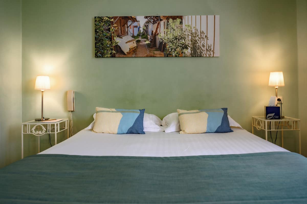 Un lit bien fait avec deux oreillers, une table de chevet avec une lampe et un tableau accroché au mur.