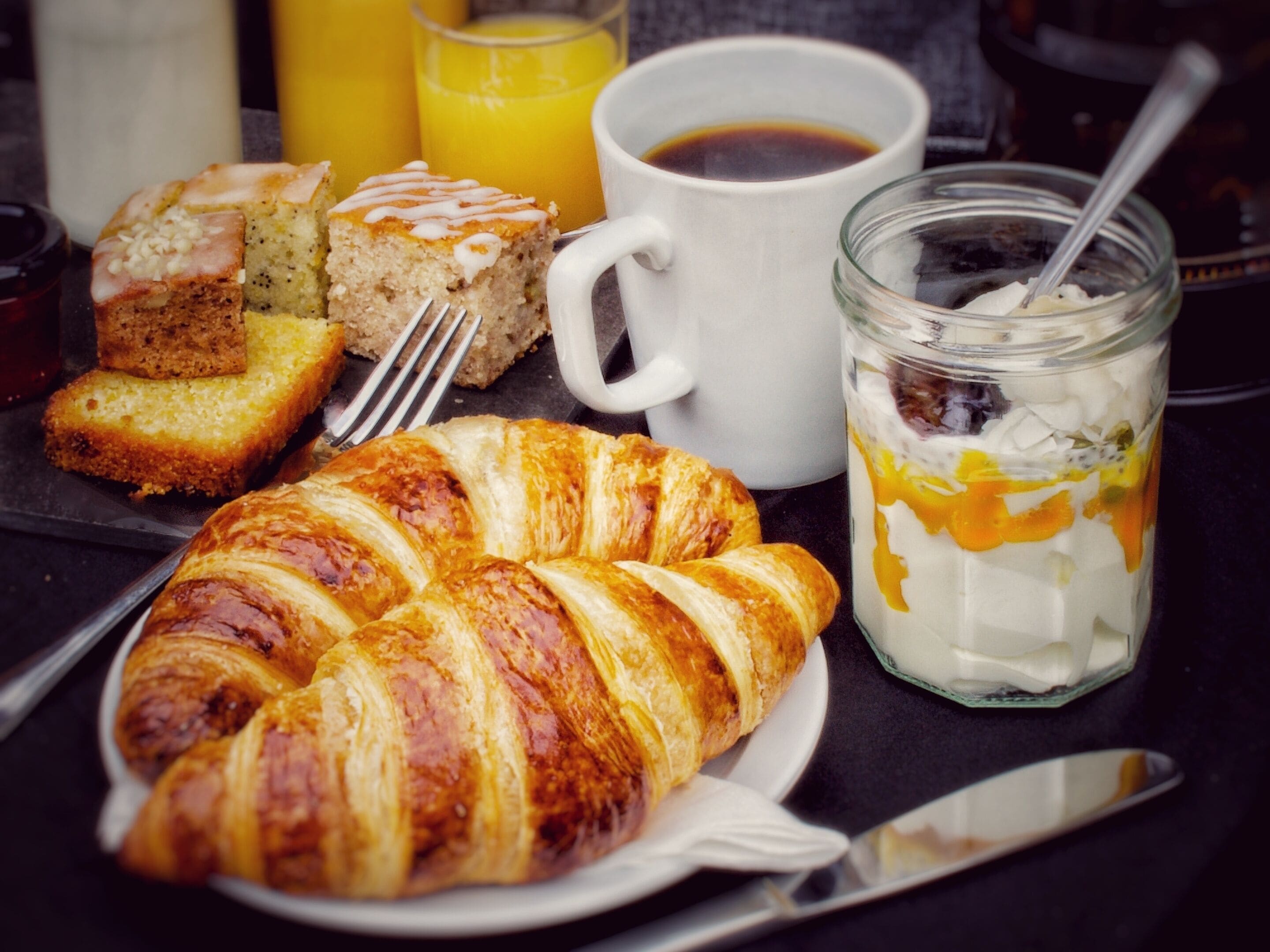 Ein Frühstückstisch mit einem Croissant, Brot, einer Tasse Kaffee und einem Glas Orangensaft.