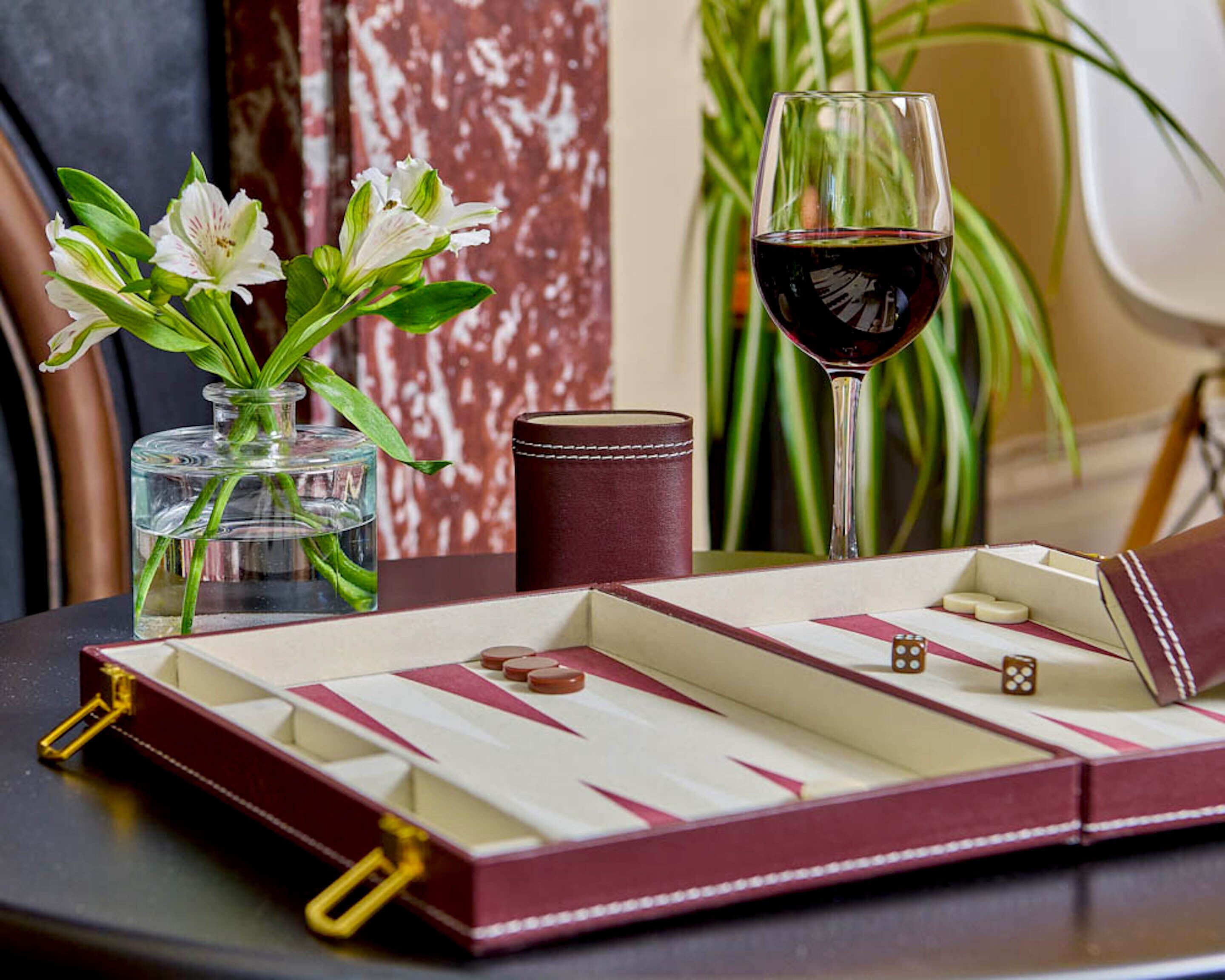Una mesa con una caja de bombones, una copa de vino tinto y un jarrón con flores blancas.