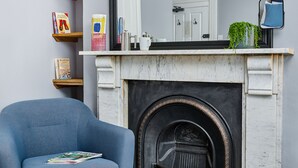 Una sala de estar con un sillón azul, una chimenea, una estantería y una mesa de centro.