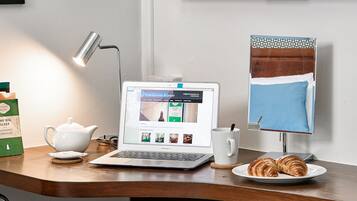 Una laptop sobre un escritorio de madera con una taza, una tetera y un plato con cruasanes.