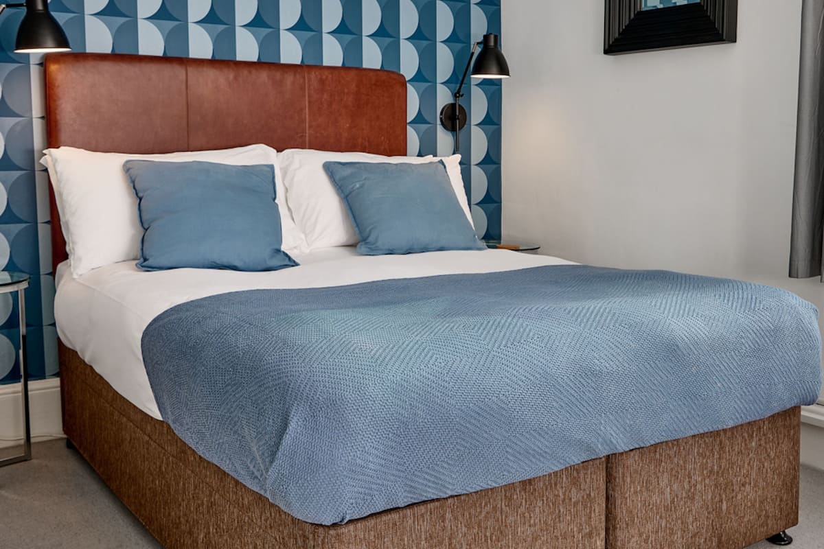 A bed with a wooden headboard, white and blue bedding, and a blue throw blanket.