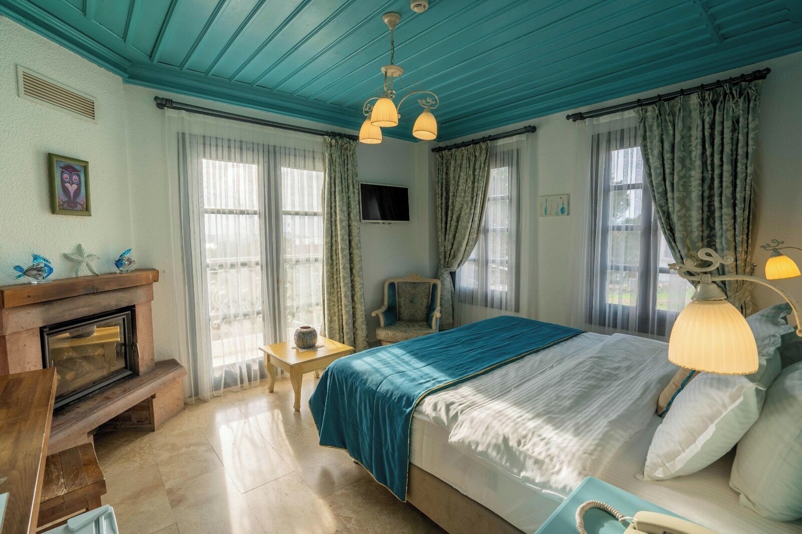 A bedroom with a bed, a wooden bench, a small table, a fireplace, and a TV on the wall.