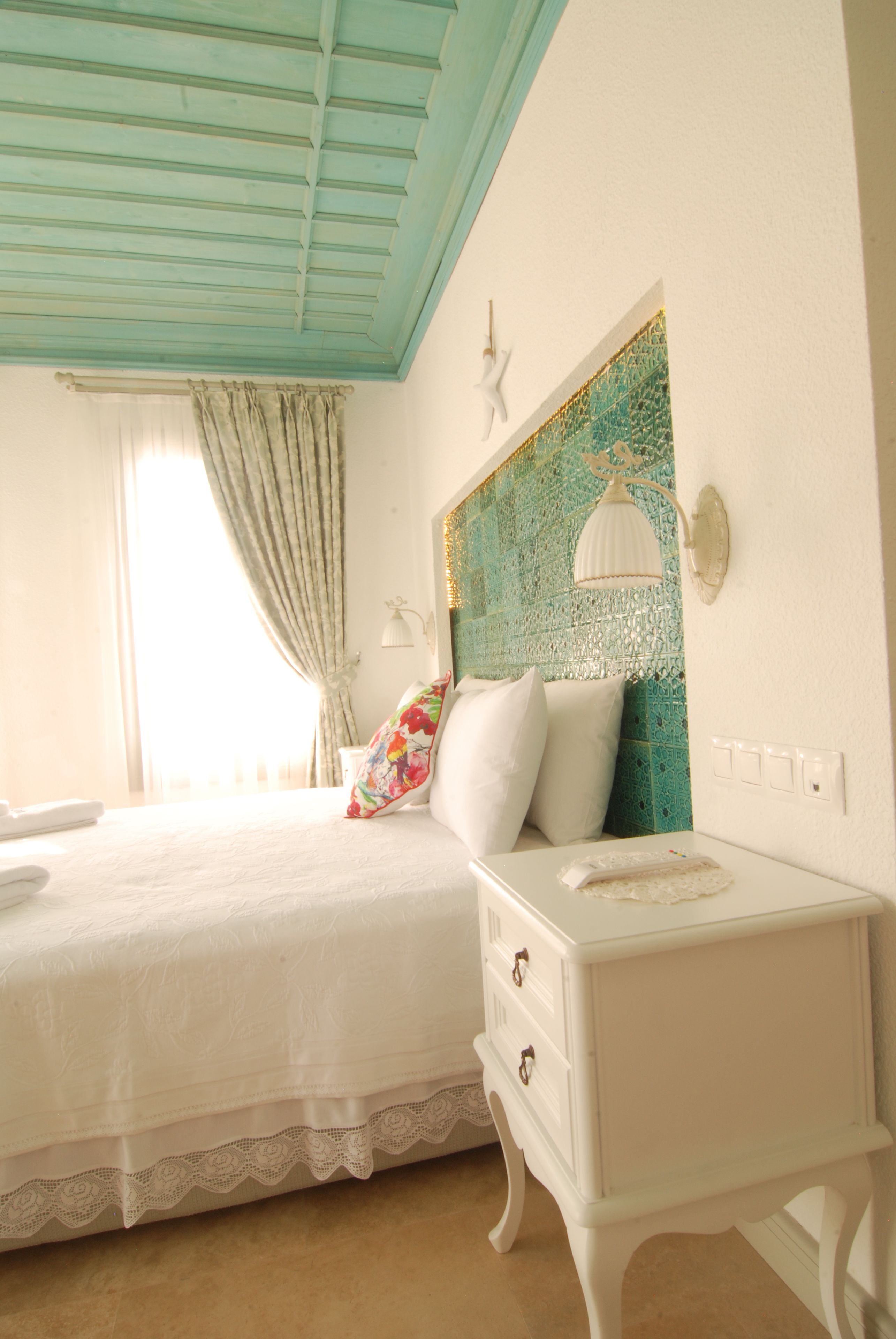 A bedroom with a bed, a nightstand, a decorative wall, and a window with curtains.