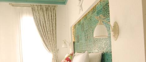 A bedroom with a bed, a nightstand, a decorative wall, and a window with curtains.