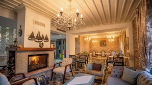 A cozy living room with a fireplace, plush seating, and a dining area with a stone wall backdrop. - Cunda Fora Hotel (Ayvalik)