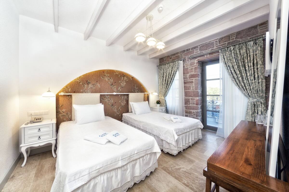 A bedroom with two beds, a wooden desk, and a stone wall.