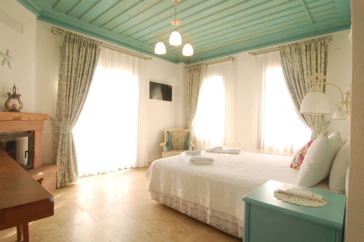 A bedroom with a bed, a chair, a nightstand, a dresser, and a window with curtains.
