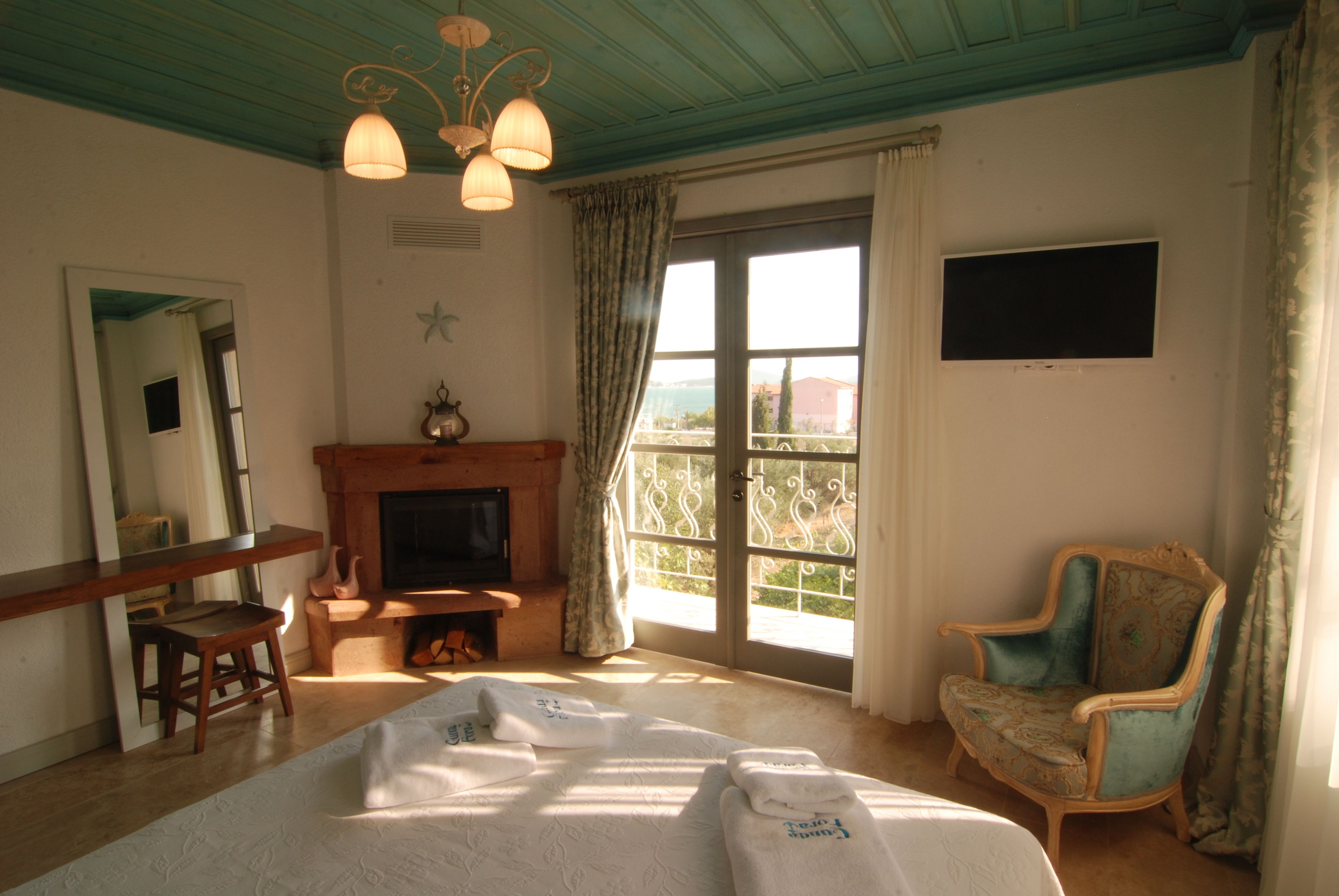 A bedroom with a bed, a wooden chair, a television, a fireplace, and a large window with curtains.