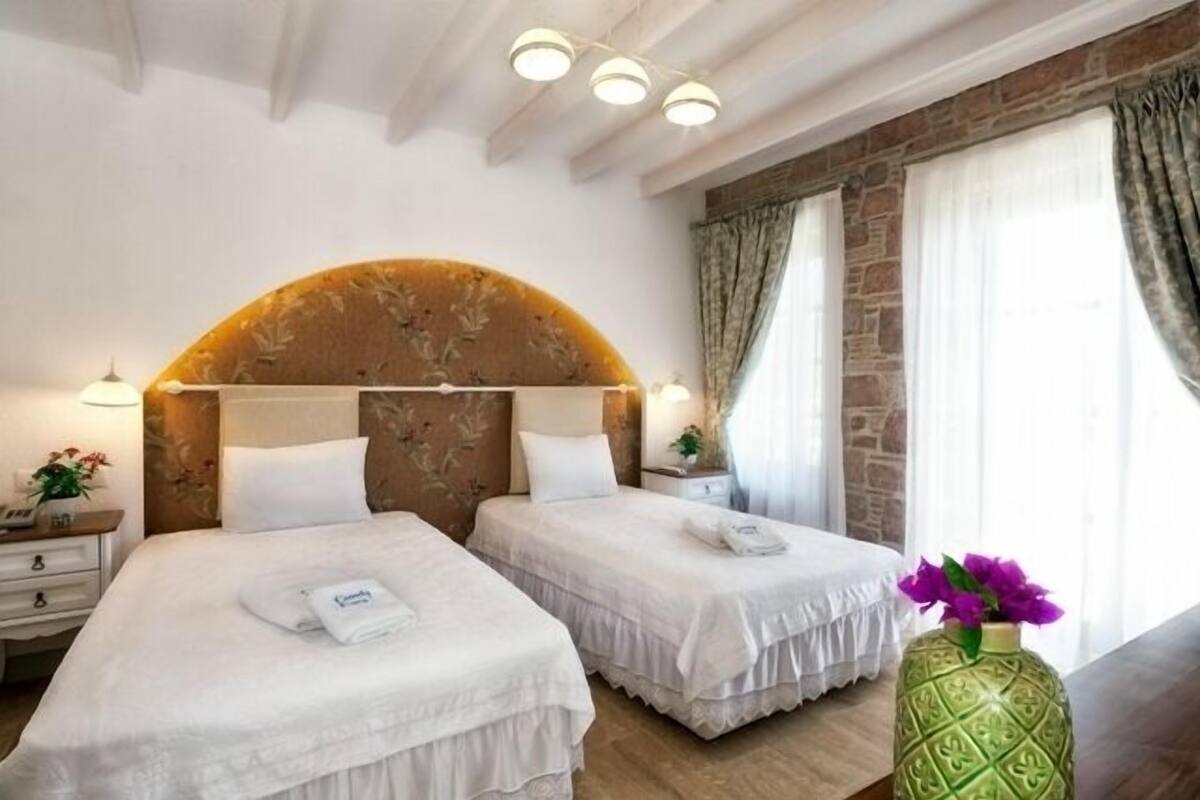 A hotel room with two beds, a stone accent wall, and a large window with curtains.
