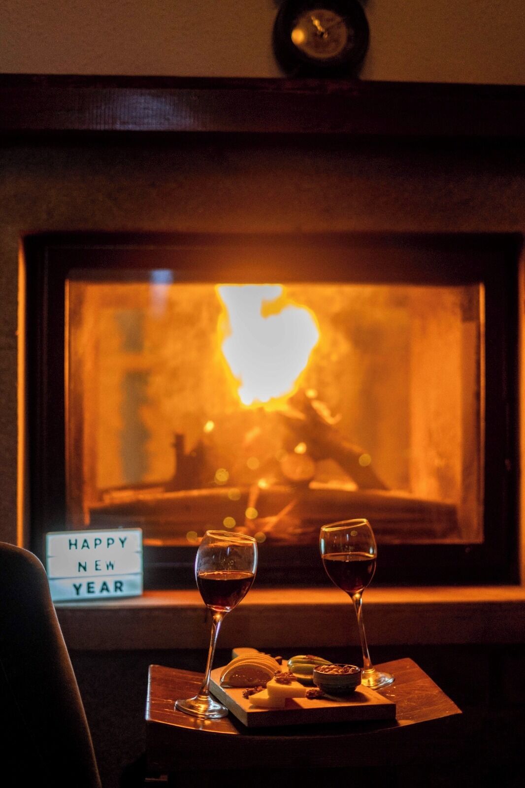 A cozy room with a fireplace, two glasses of wine, and a 'Happy New Year' sign.
