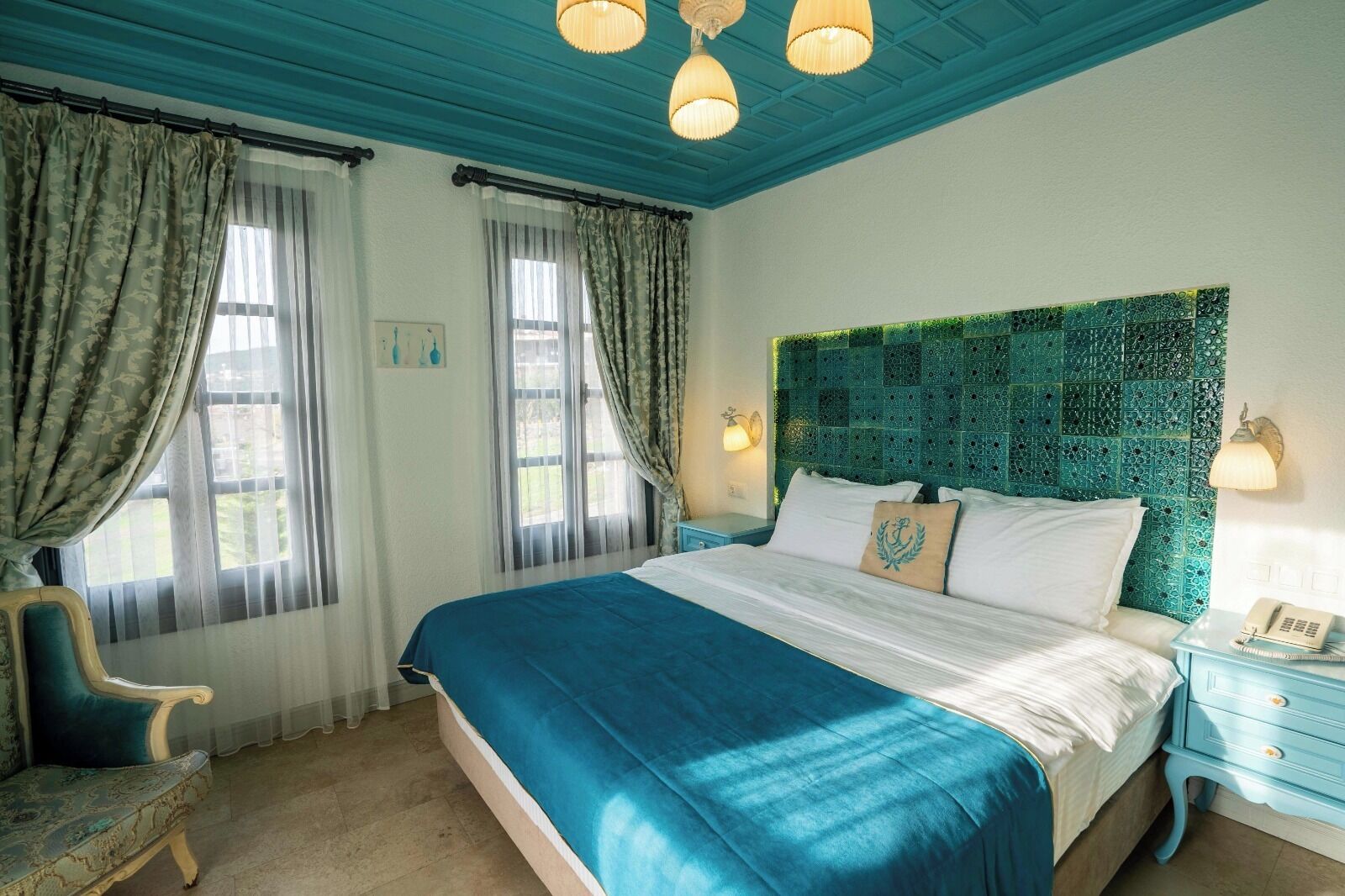 A bedroom with a large bed, a headboard with a mosaic pattern, a chair, and a nightstand with a phone.