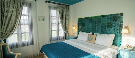 A bedroom with a large bed, a headboard with a mosaic pattern, a chair, and a nightstand with a phone.
