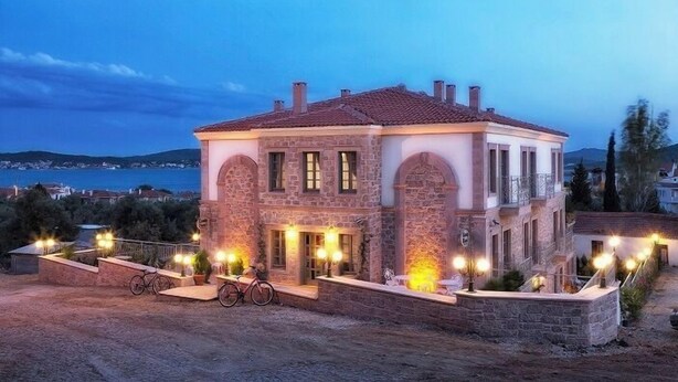 A stone building with a tiled roof, arched windows, and a paved driveway with a bicycle. - Cunda Fora Hotel (Ayvalik)