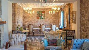 A cozy room with a stone wall, a chandelier, and a dining area with chairs and a table. - Cunda Fora Hotel (Ayvalik)