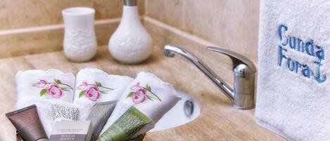 Une salle de bain avec un lavabo, un panier rempli d’articles de toilette et une serviette ornée d’une broderie « Sunda Fura ».