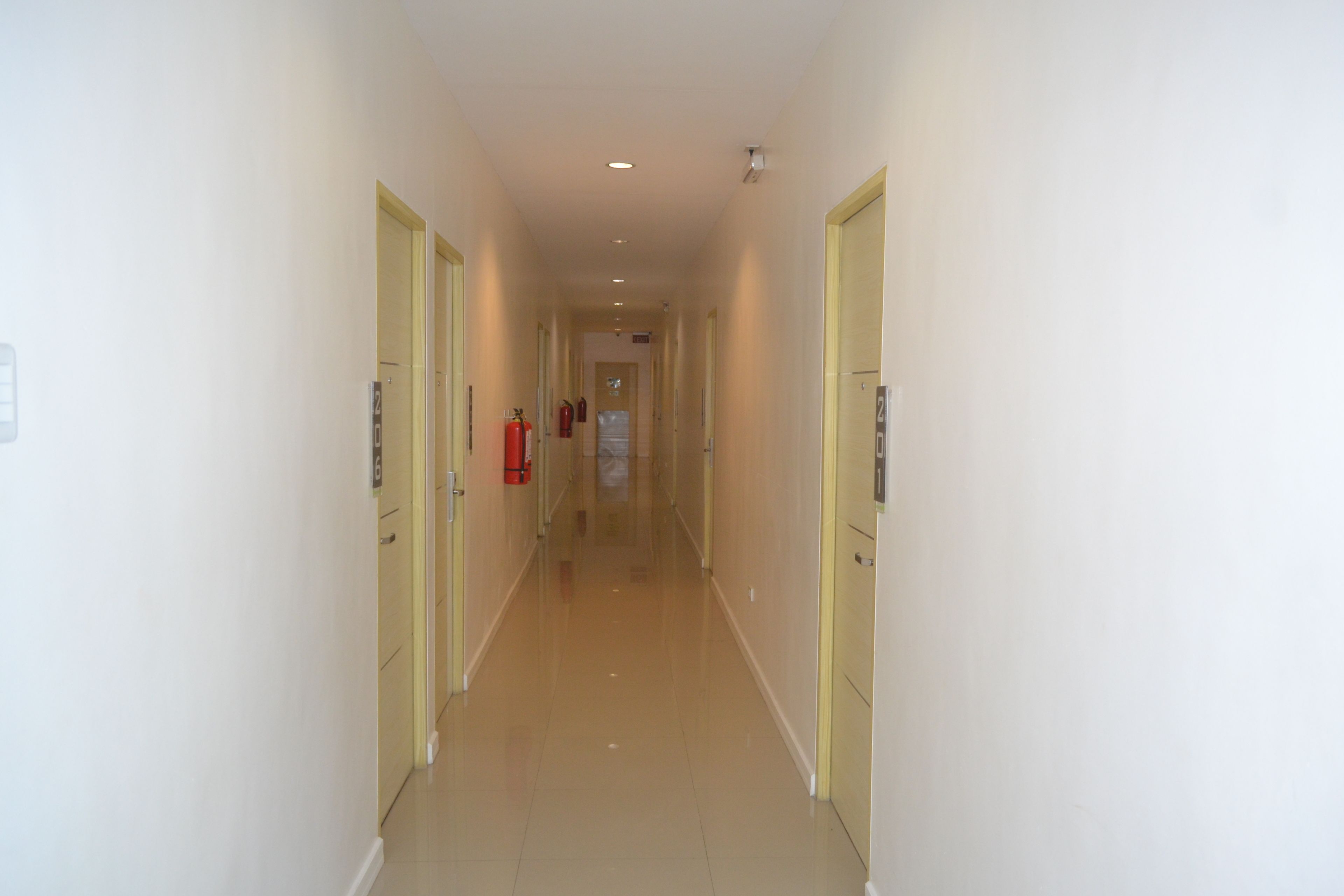 A long, narrow hallway with cream-colored walls and doors, leading to a room at the end.