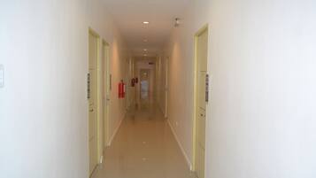 A long, narrow hallway with cream-colored walls and doors, leading to a room at the end.