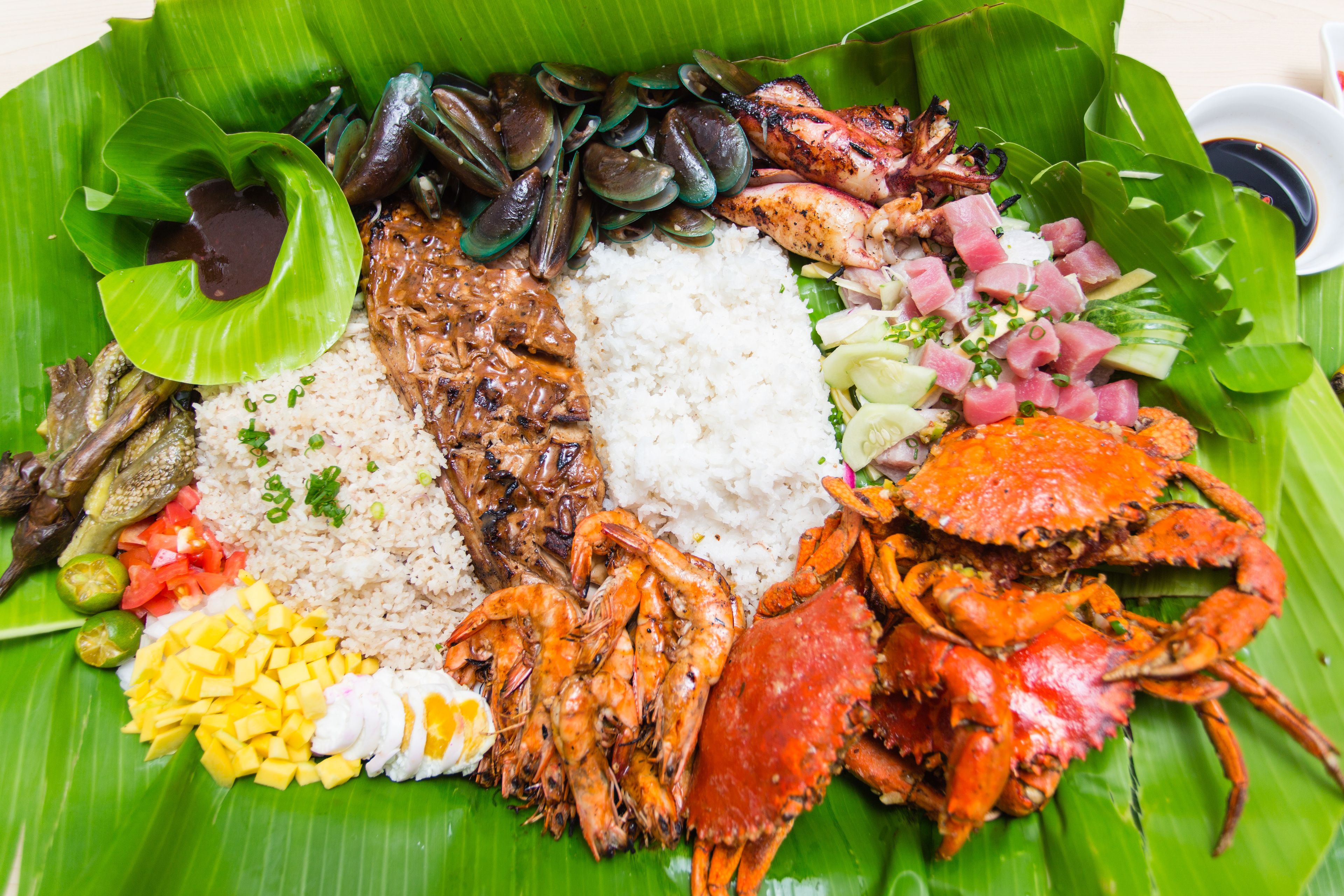 A variety of seafood and rice dishes served on a banana leaf.