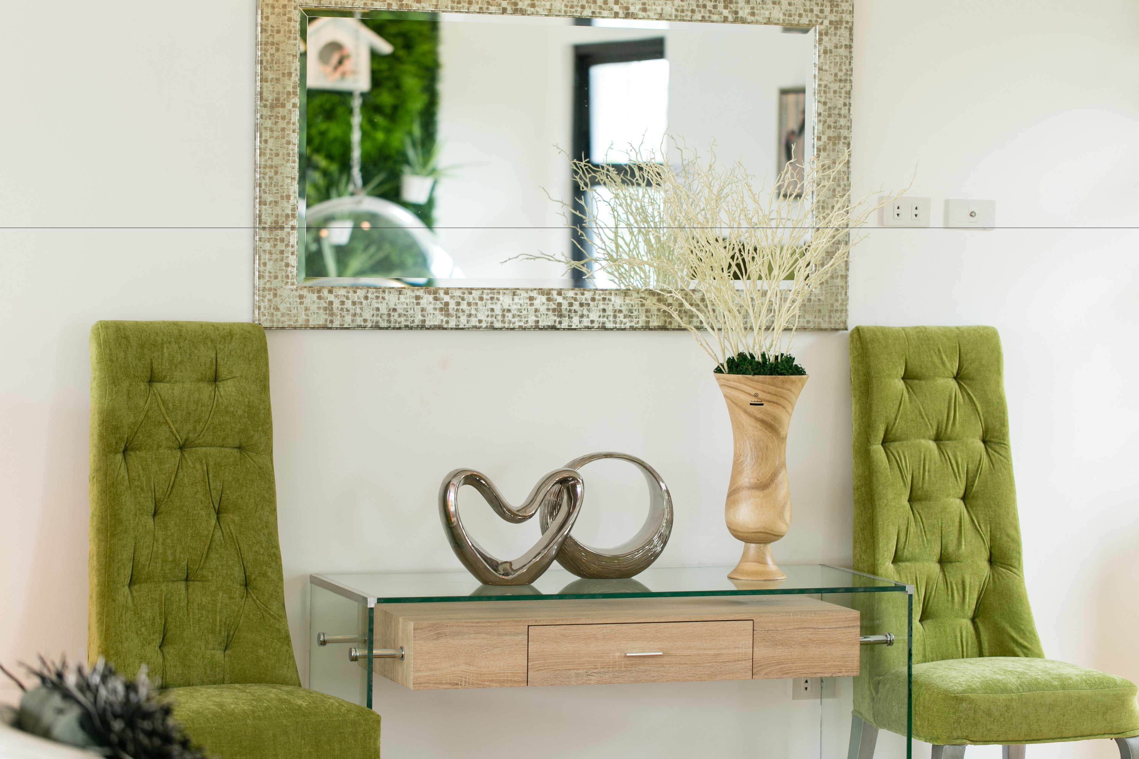Una habitación con dos sillones tapizados en verde, una mesa de centro de vidrio con base de madera y un objeto decorativo con forma de corazón.