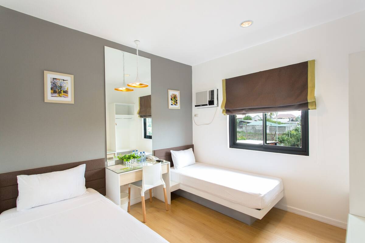 A hotel room with two beds, a desk, a chair, a large mirror, and a window with a view.