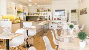 Un restaurant moderne avec des meubles blancs, un coin bar et un téléviseur fixé au mur.