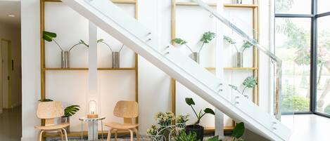 Un interior moderno con una escalera de cristal, sillas de madera y plantas en macetas.