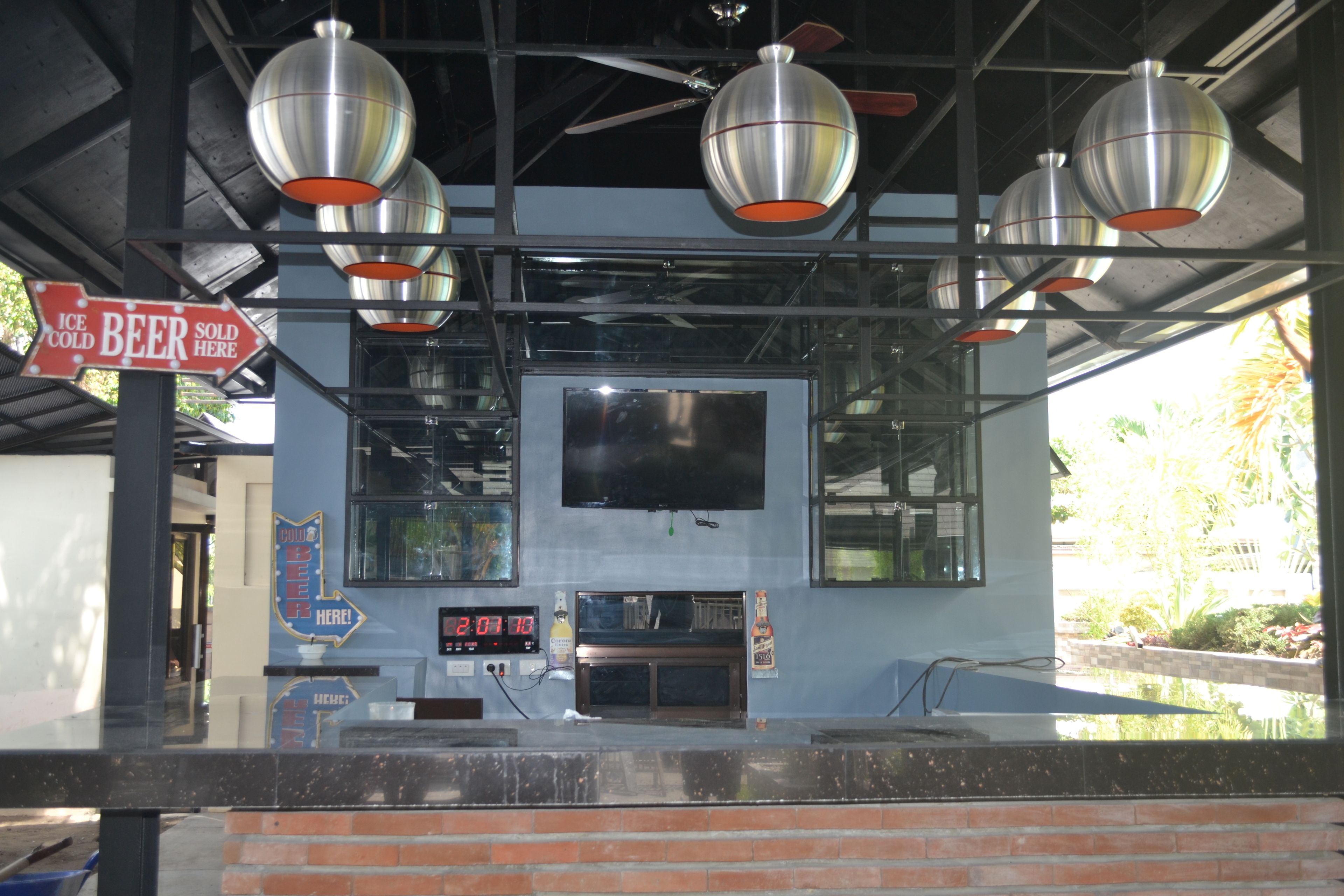 Una zona de bar con un reloj digital, luces colgantes y carteles que anuncian cerveza bien fría.