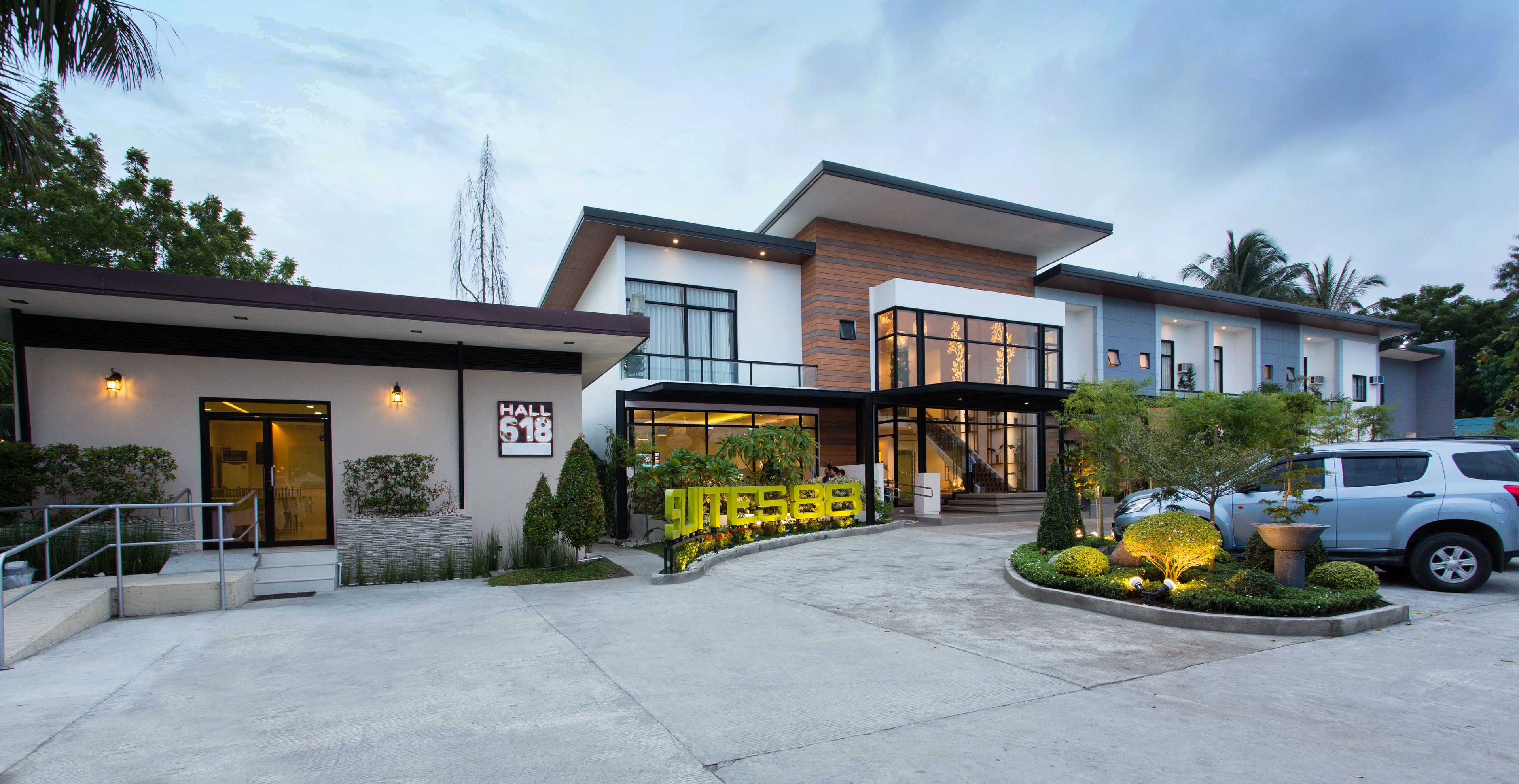 A modern hotel with a glass facade, a well-lit entrance, and a landscaped garden area.