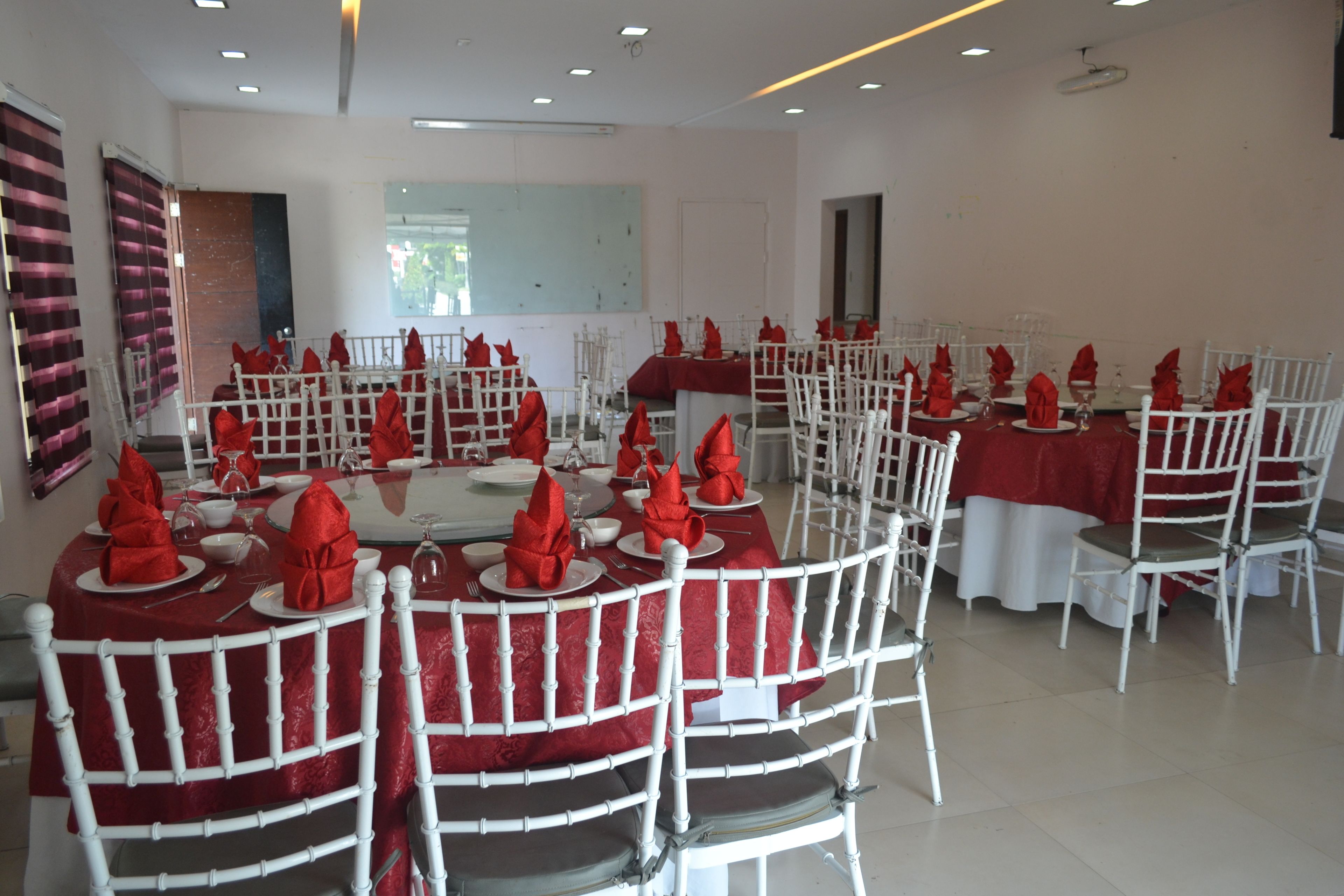 Un salón de banquetes con mesas redondas, sillas blancas y servilletas rojas.