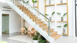 Un escalier moderne avec des rampes en verre et des marches à motifs, flanqué de chaises en bois et de plantes en pot.