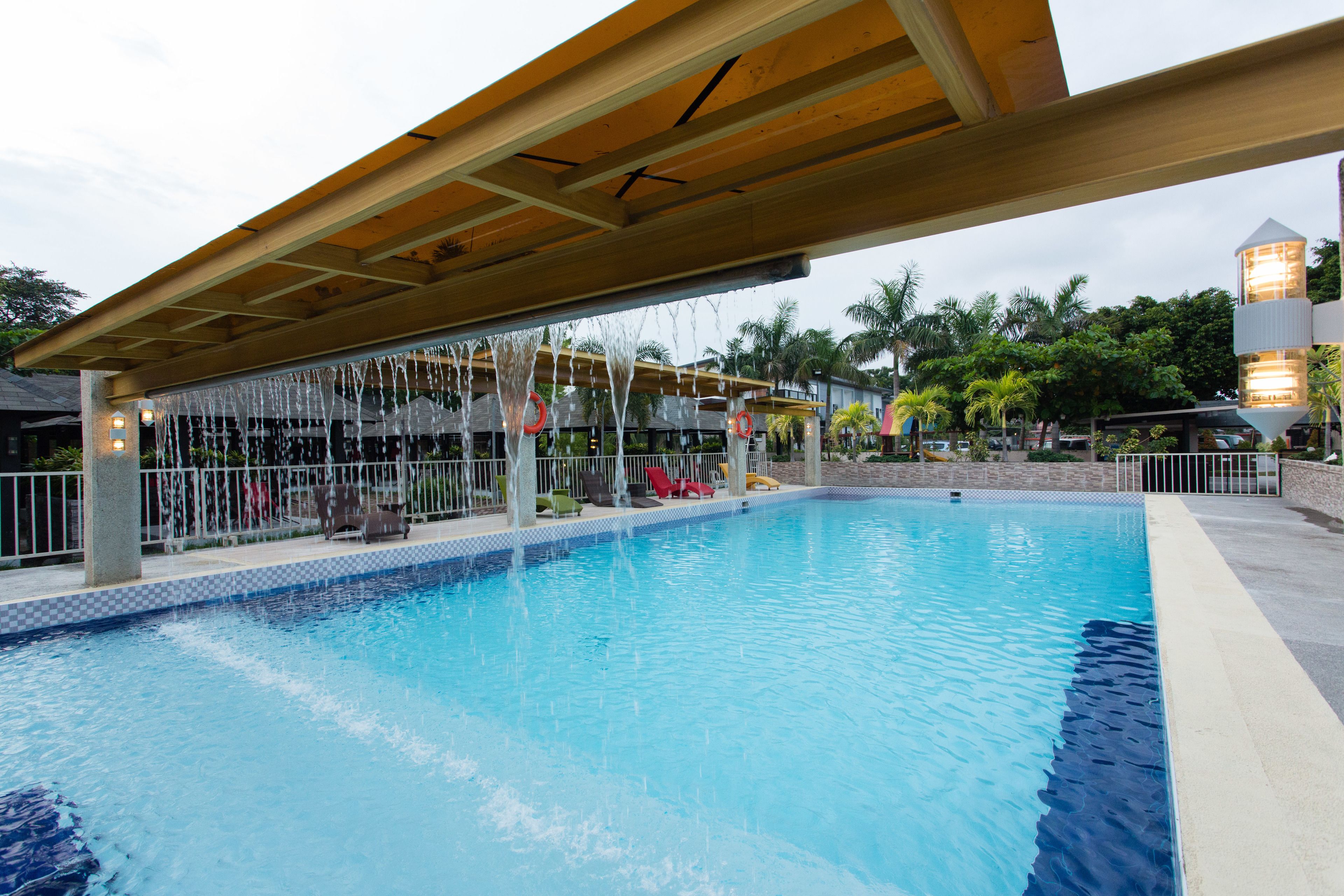 A swimming pool with a wooden canopy overhead, surrounded by a fence and various seating areas.