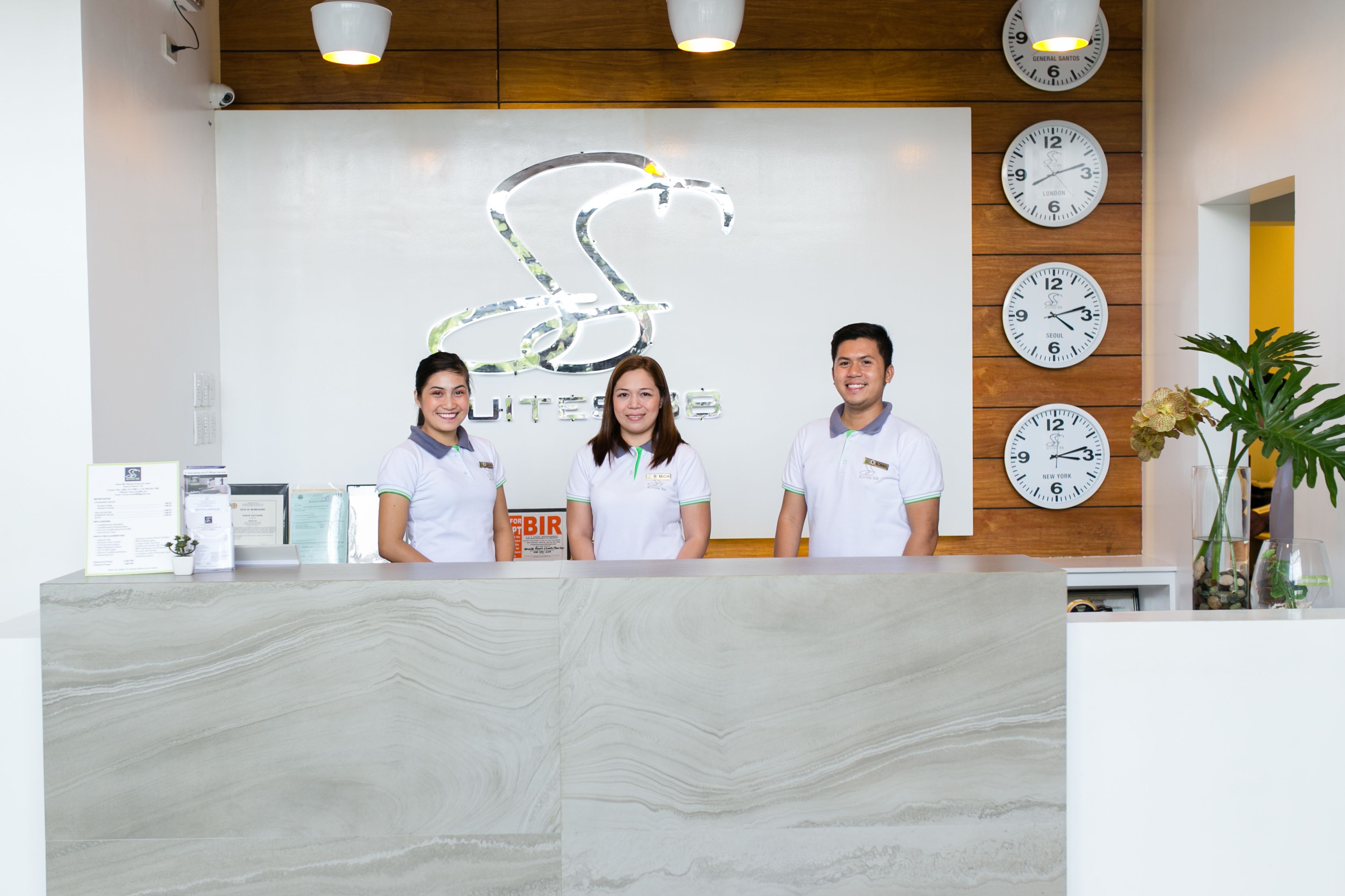 A reception desk with three staff members, a large decorative wall with clocks, and a sign that reads "BIR".