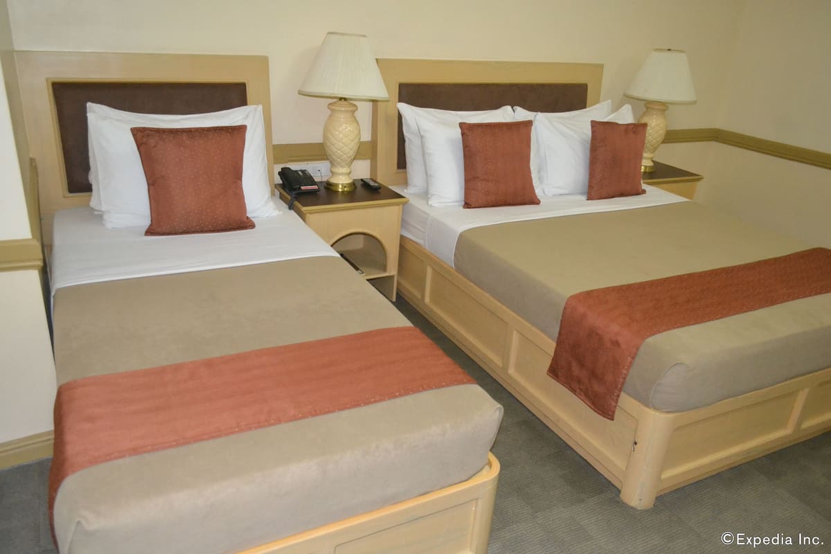 Duas camas de solteiro com roupa de cama bege e castanho, mesas de cabeceira com abajures e um telefone em uma das mesas.