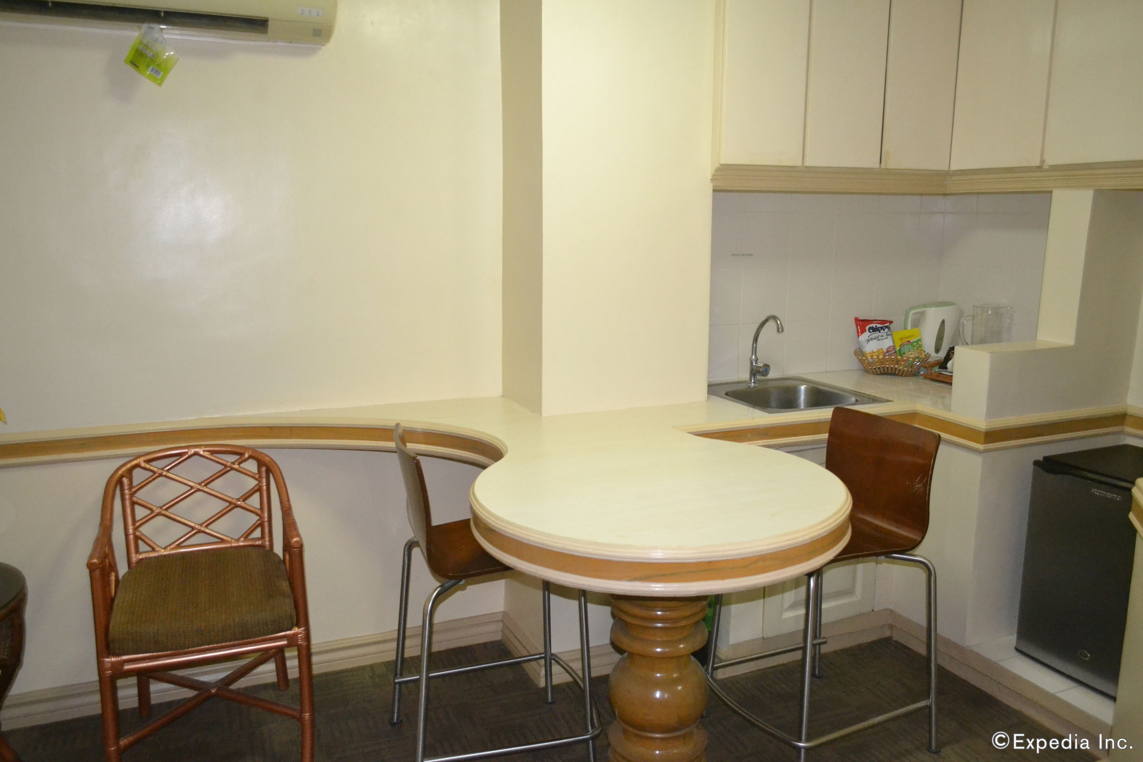 A compact kitchen with a round table, two chairs, a sink, and a refrigerator.