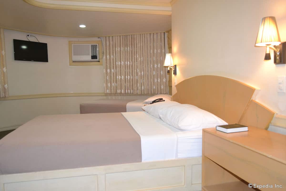 Quarto de hotel com cama, mesa de cabeceira, abajur, televisão, aparelho de ar condicionado e cortinas.