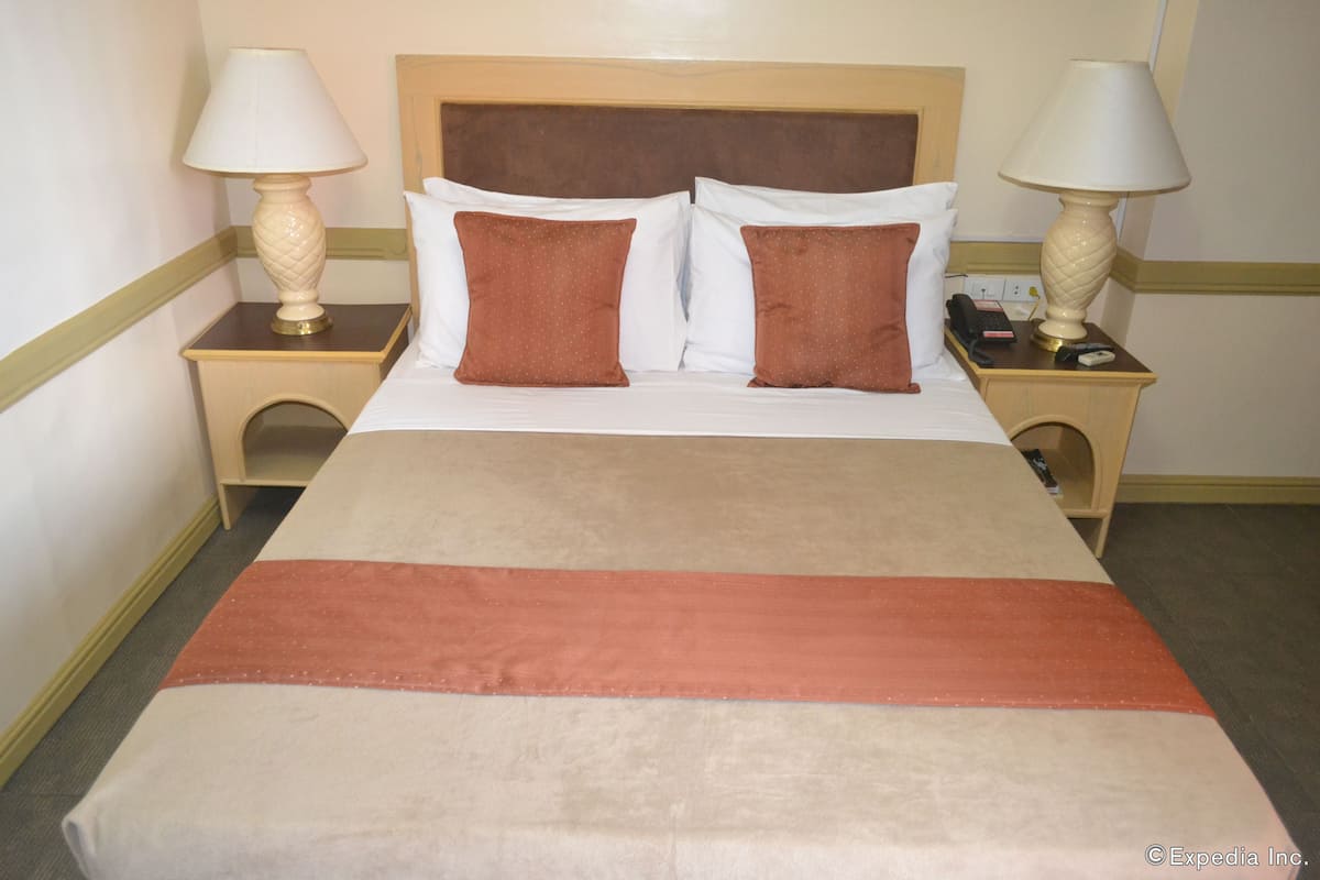Quarto de hotel com uma cama, duas mesas de cabeceira com luminárias e um telefone em uma delas.