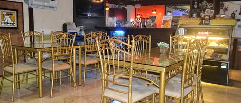 Un restaurante con una mesa de vidrio y sillas doradas, una barra con productos horneados y un techo decorativo.