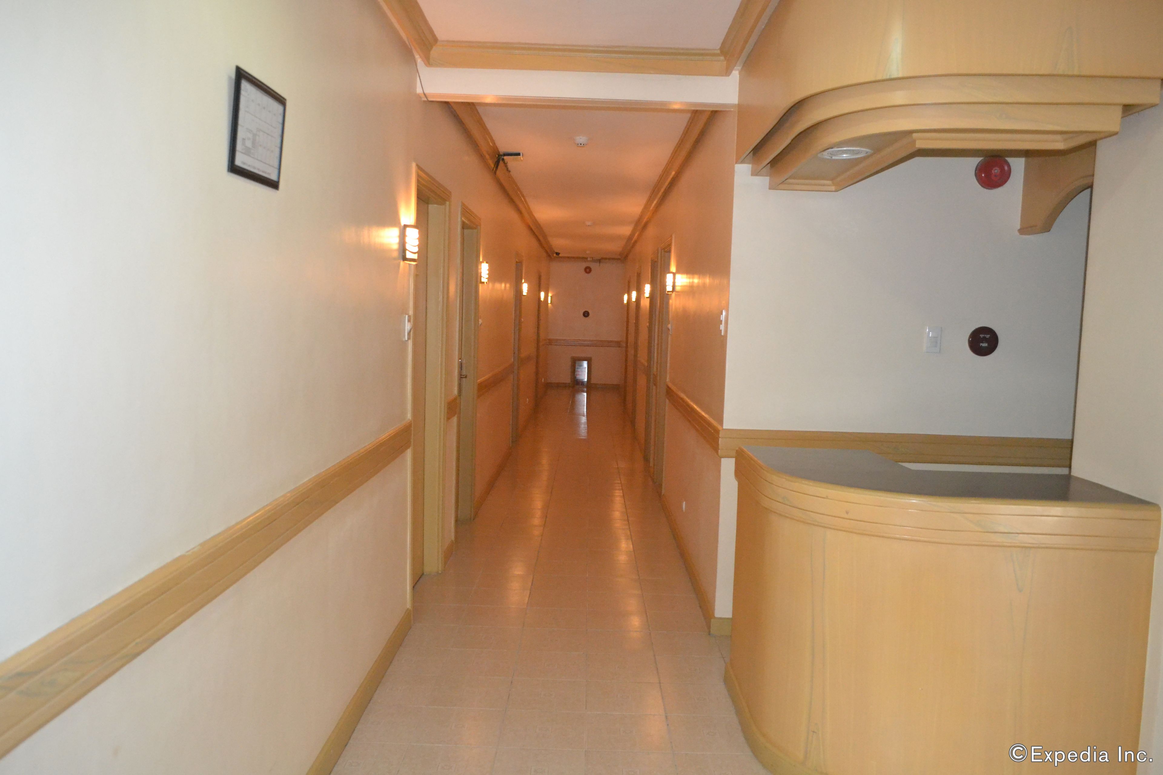 A hotel hallway with a wooden reception desk, light-colored walls, and a framed picture on the wall.