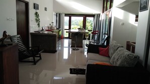 Amplia sala de estar con techo alto, comedor con cocina y ventanas grandes que ofrecen vistas a zonas verdes.