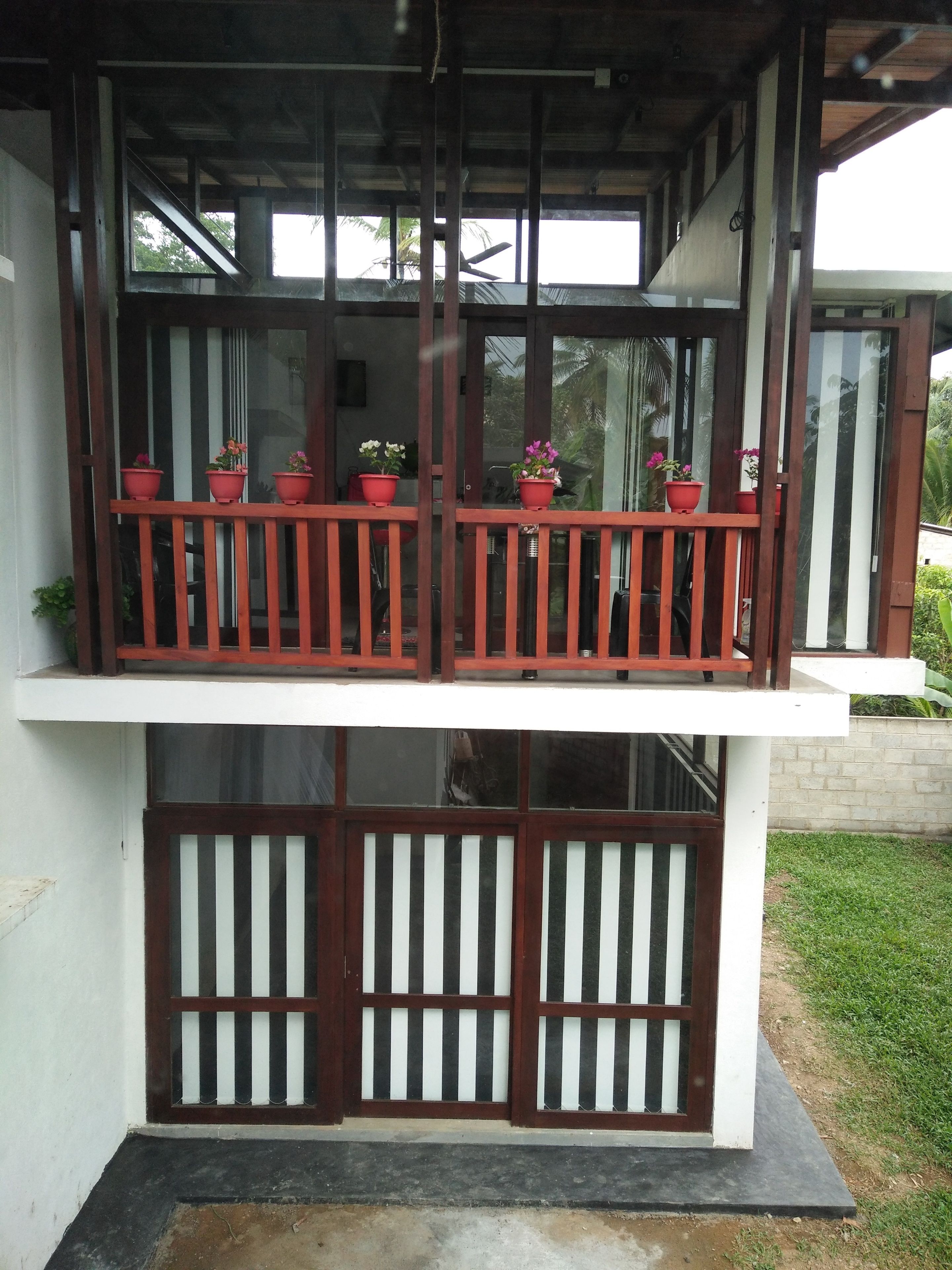 A two-story building with a balcony on the upper floor, featuring a wooden railing and potted plants.